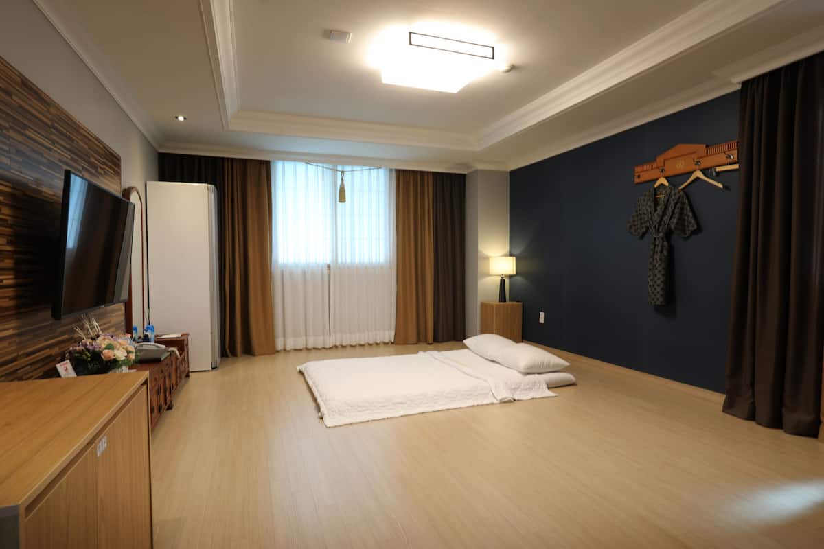 Quarto de hotel com cama, televisão, secretária, abajur e guarda-roupa.