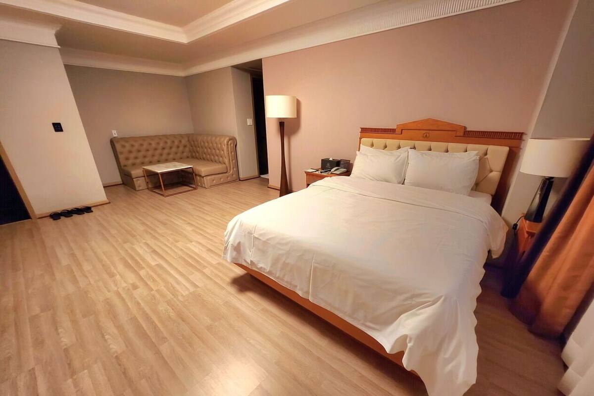 Quarto de hotel com uma cama grande, um sofá, uma mesa de cabeceira e uma luminária.
