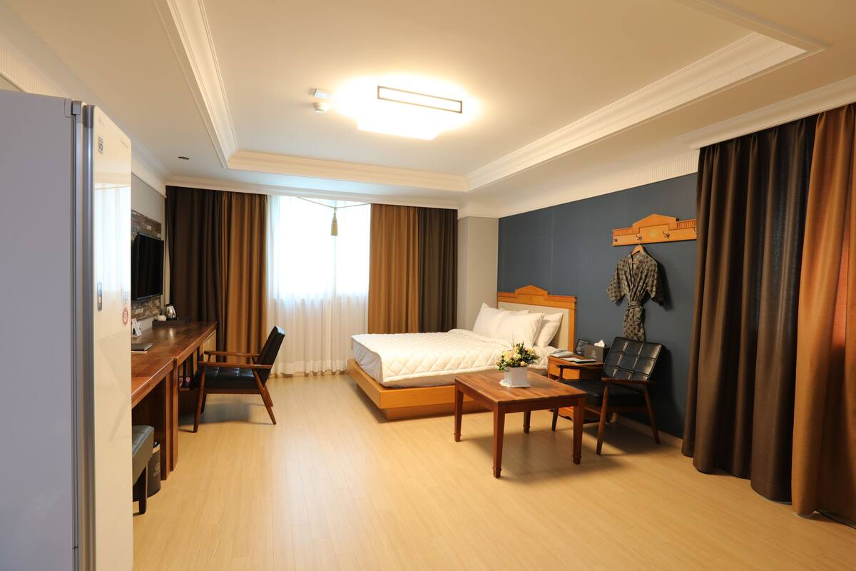 Quarto de hotel com cama, escrivaninha, cadeira, televisão e janela com cortinas.