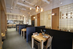 A modern dining area with wooden tables and black partitions, featuring pendant lighting and a visible kitchen area in the background.