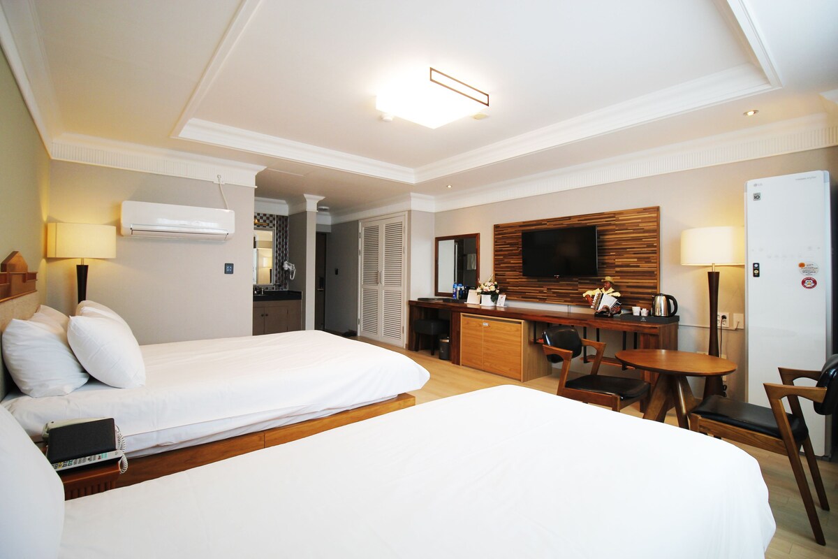 A hotel room with two beds, a desk, a television, and a refrigerator.