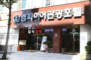 A hotel entrance with a sign in Korean, a potted plant, and a glass door.