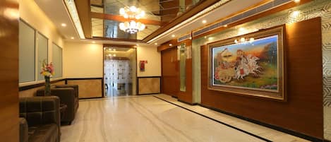 A spacious lobby with a marble floor, a chandelier, and a large mural on the wall.