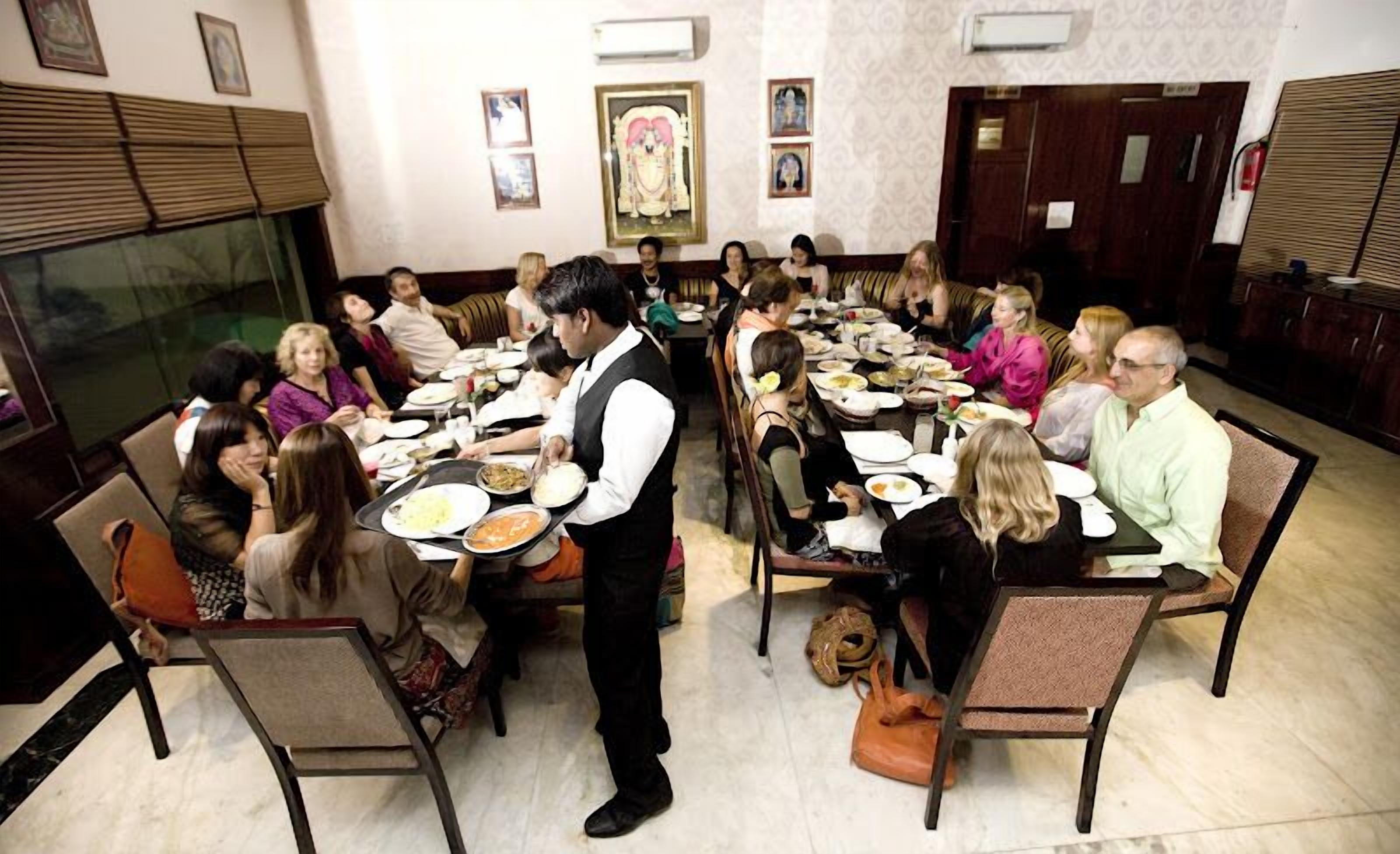 A dining hall with round tables, guests seated, and a waiter serving food.