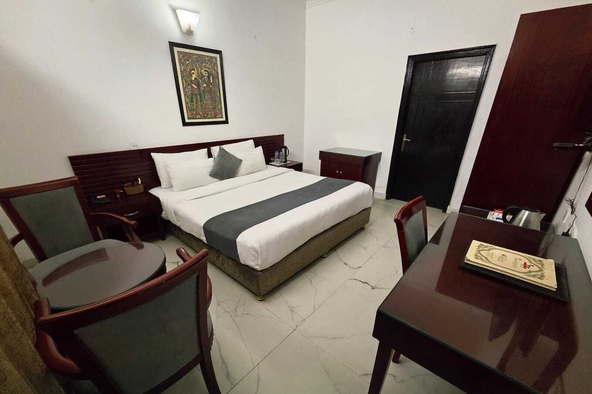 Habitación de hotel con cama, escritorio, silla, mesita de noche y una puerta.