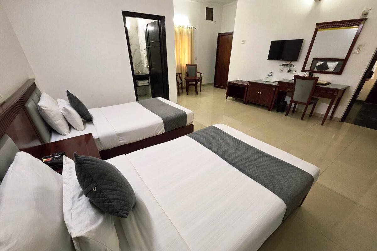 Habitación de hotel con dos camas, un escritorio, una silla, un televisor y un espejo.