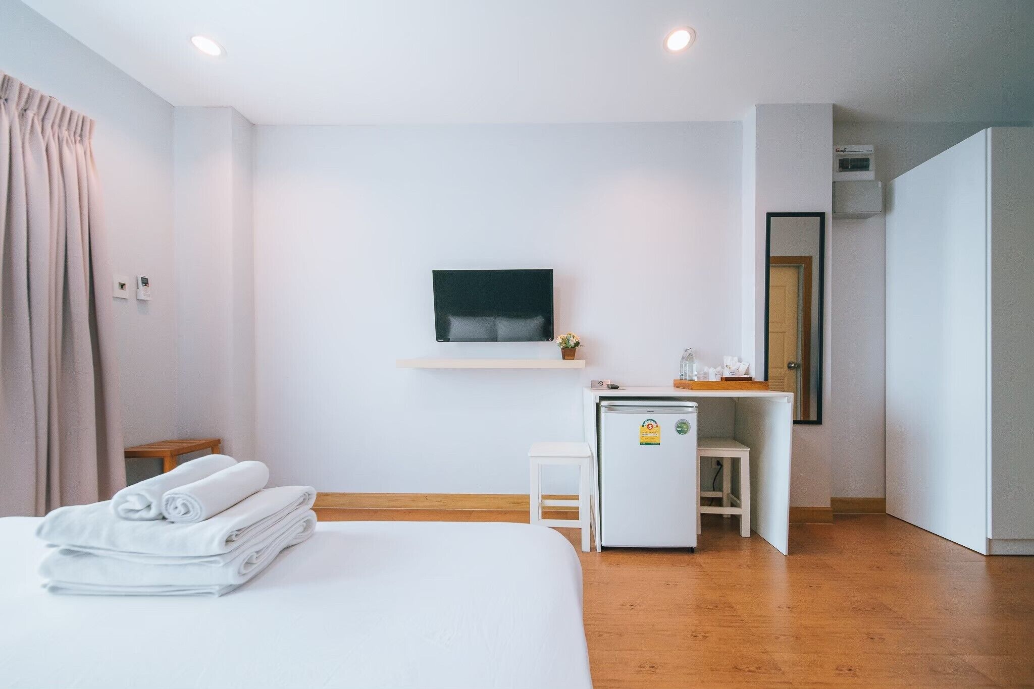 A hotel room with a bed, a small desk with a refrigerator, a television mounted on the wall, and a wooden floor.