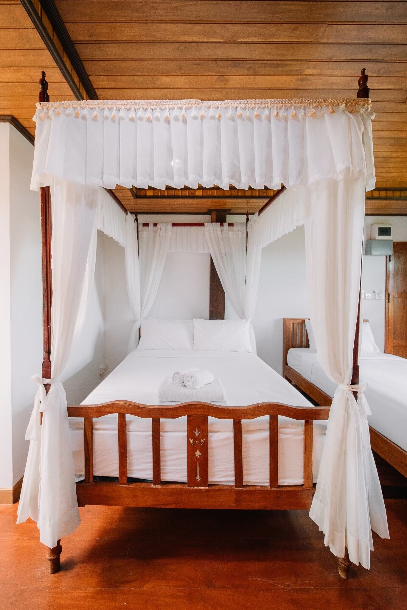 A four-poster canopy bed with white linens and curtains, wooden headboard, and a wooden floor.