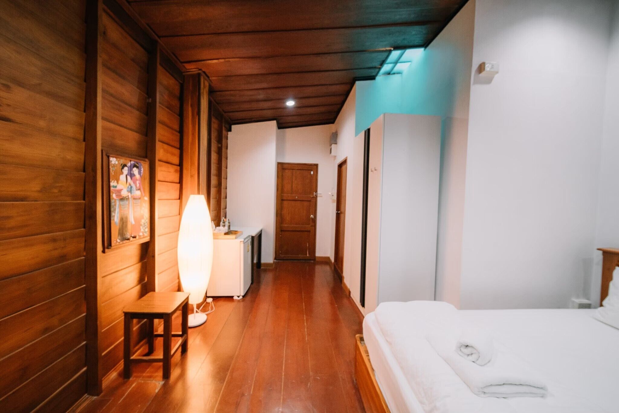 Een smalle gang met houten wanden en een houten plafond, die leidt naar een slaapkamer met een bed en nachtkastje.