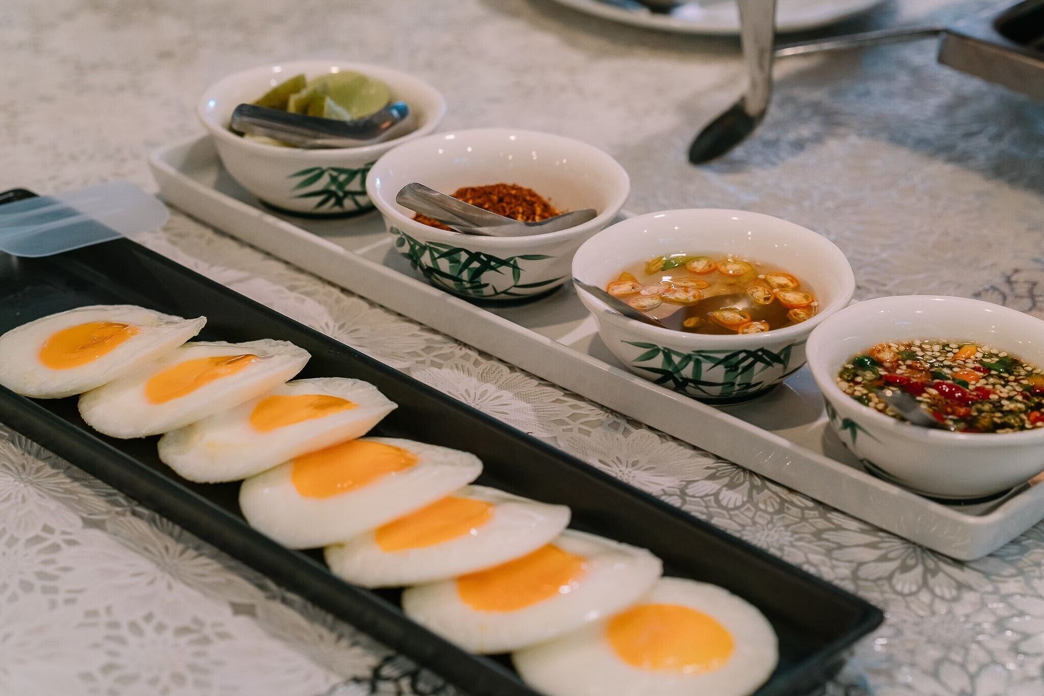 Una bandeja con cinco huevos fritos y cuatro recipientes pequeños con condimentos.