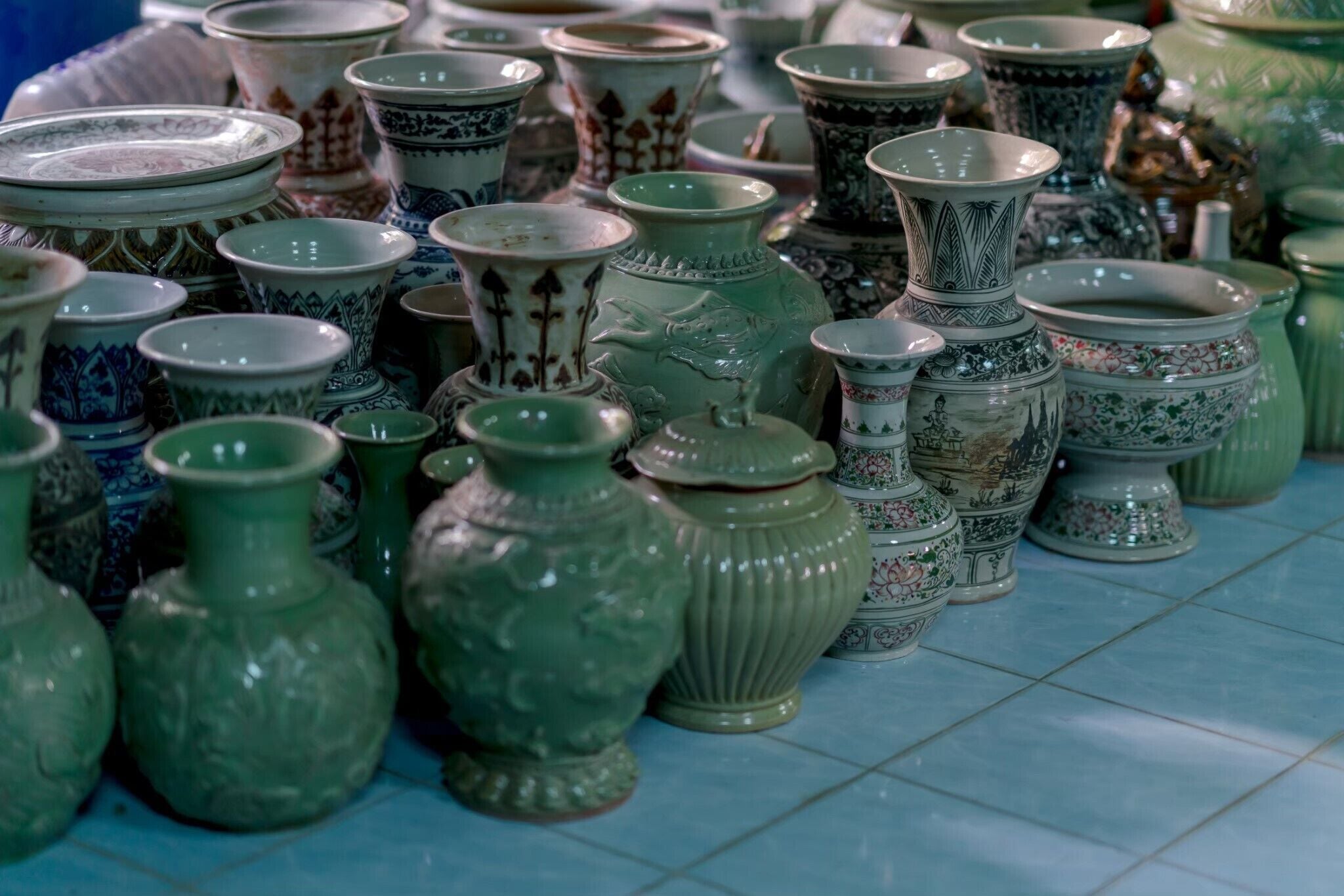 A variety of ceramic vases and bowls arranged on a tiled floor.