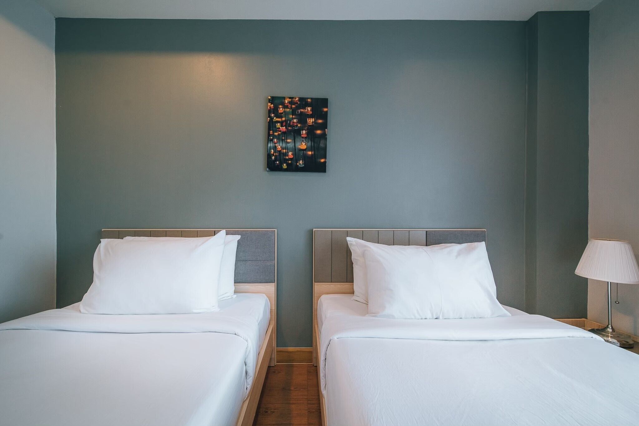 A hotel room with two beds, a nightstand, a lamp, and a wall-mounted artwork.