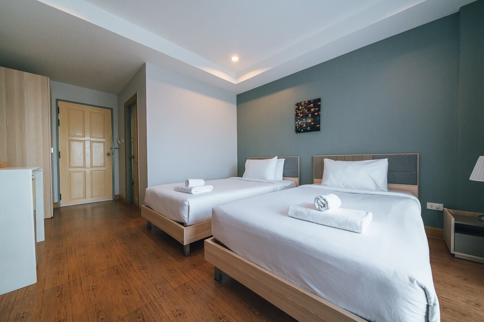 Hotellihuone, jossa on kaksi sänkyä, puulattia, vaatekaappi ja seinälle ripustettu taideteos.