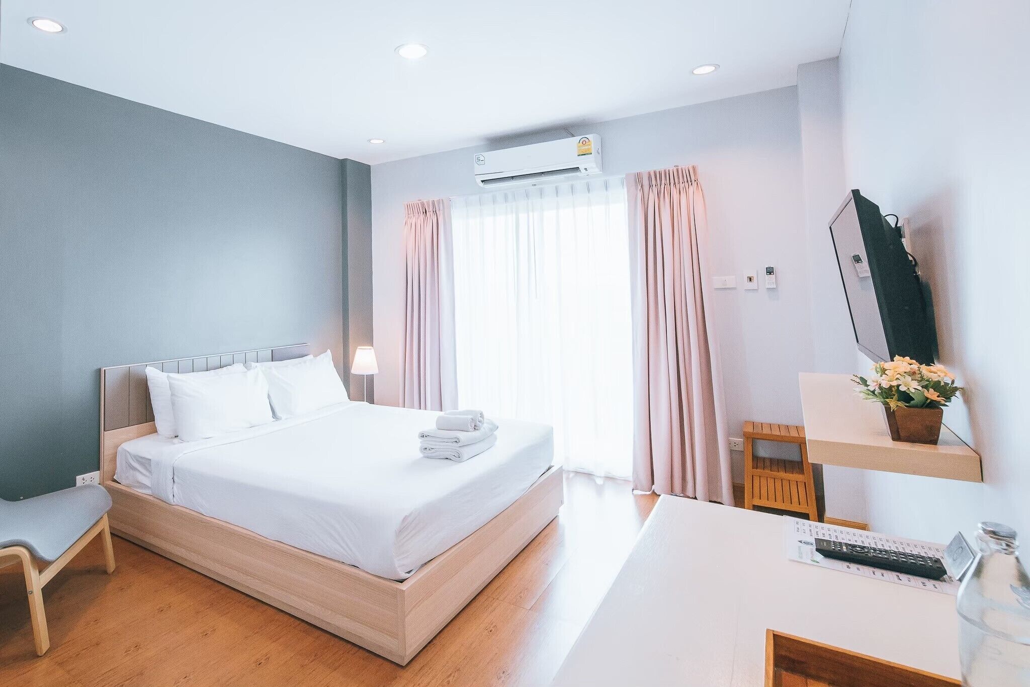 Quarto de hotel moderno com uma cama de madeira, uma escrivaninha com um computador, uma cadeira e uma janela com cortinas.