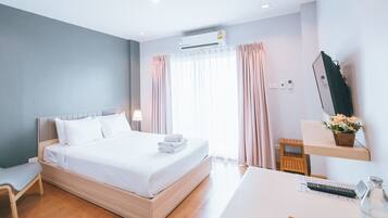 Quarto de hotel moderno com uma cama de madeira, uma escrivaninha com um computador, uma cadeira e uma janela com cortinas.