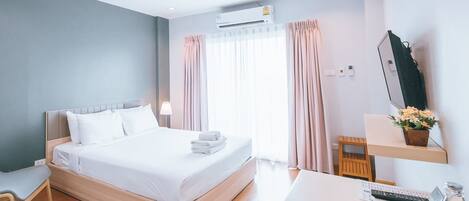 A modern hotel room with a wooden bed, a desk with a computer, a chair, and a window with curtains.