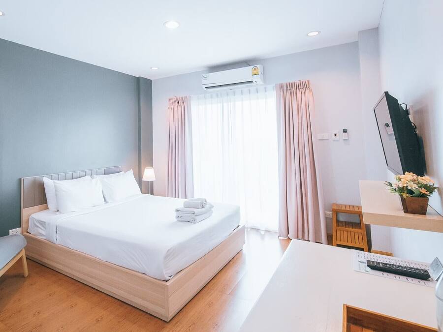 Habitació d'hotel moderna amb un llit de fusta, una taula amb un ordinador, una cadira i una finestra amb cortines.