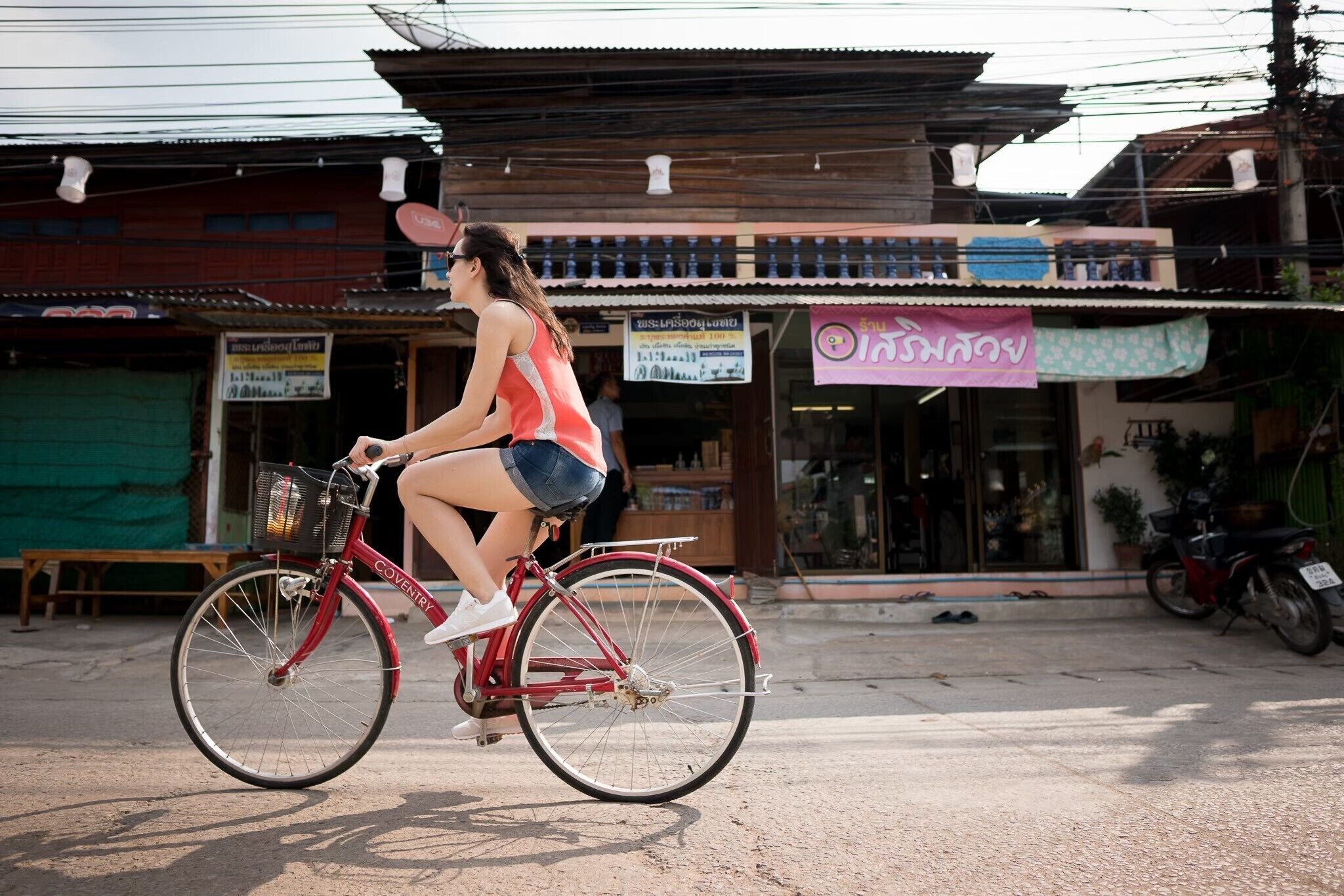 A woman riding a bicycle on a street with buildings and shops in the background.