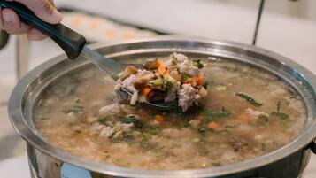 Uma pessoa mexendo uma panela de sopa com ingredientes visíveis como carne, cenouras e ervas.
