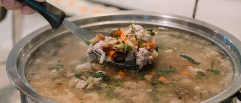 Una persona mescola una pentola di zuppa con ingredienti visibili, come carne, carote e erbe aromatiche.