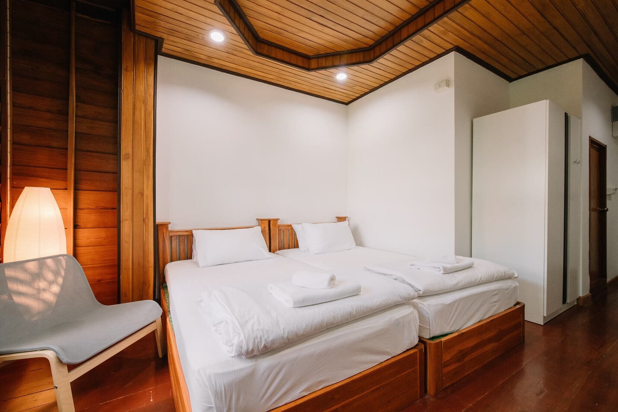 Een slaapkamer met twee bedden, houten hoofdborden, een houten plafond en een witte kledingkast.