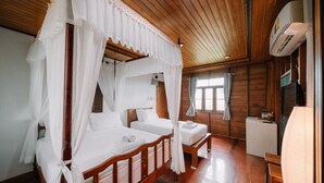 A room with two wooden beds, each with white linens and a canopy. There is a small table and a chair, and an air conditioning unit mounted on the wall. - Sukhothai Garden (Sukhothai)