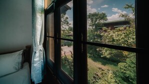 A room with a bed, a window with a view of a garden and a building outside. - Sukhothai Garden (Sukhothai)