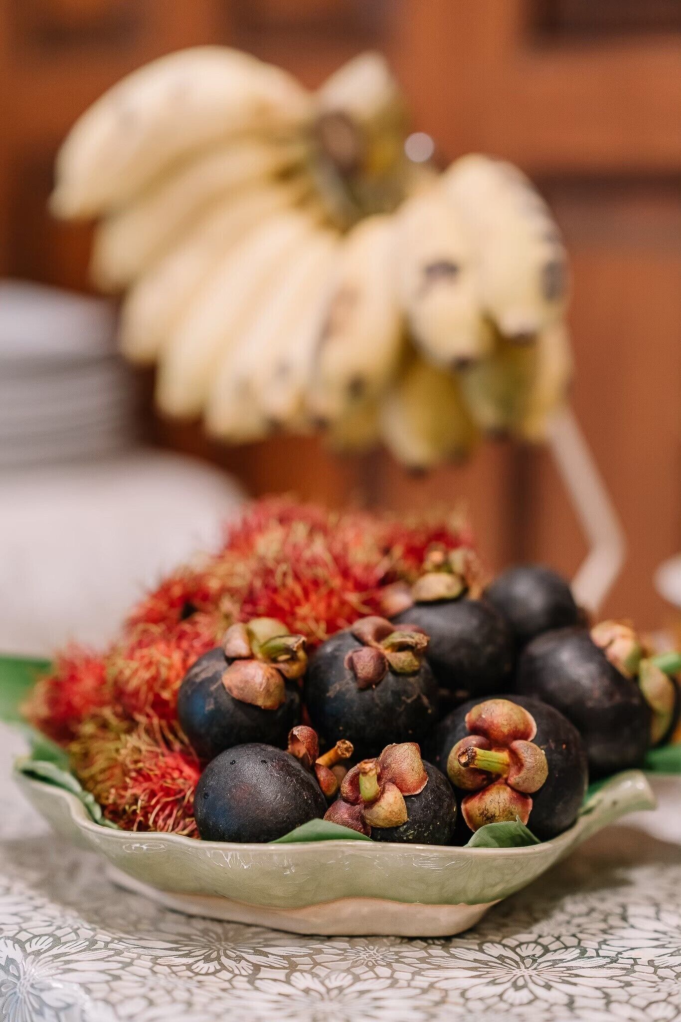 A bowl of rambutans and bananas on a patterned tablecloth.