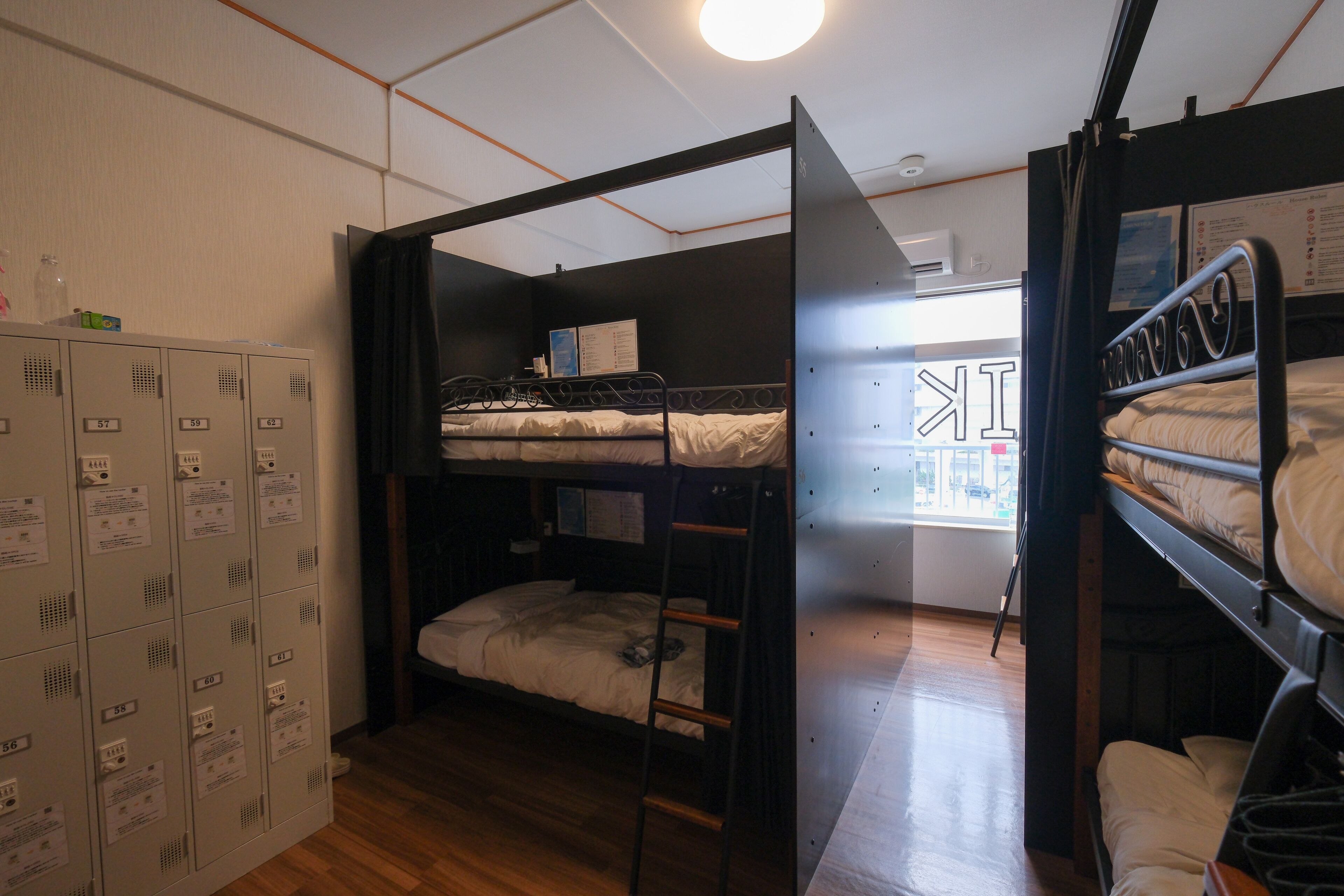 A dormitory room with bunk beds, a wooden floor, and a set of lockers on the left.