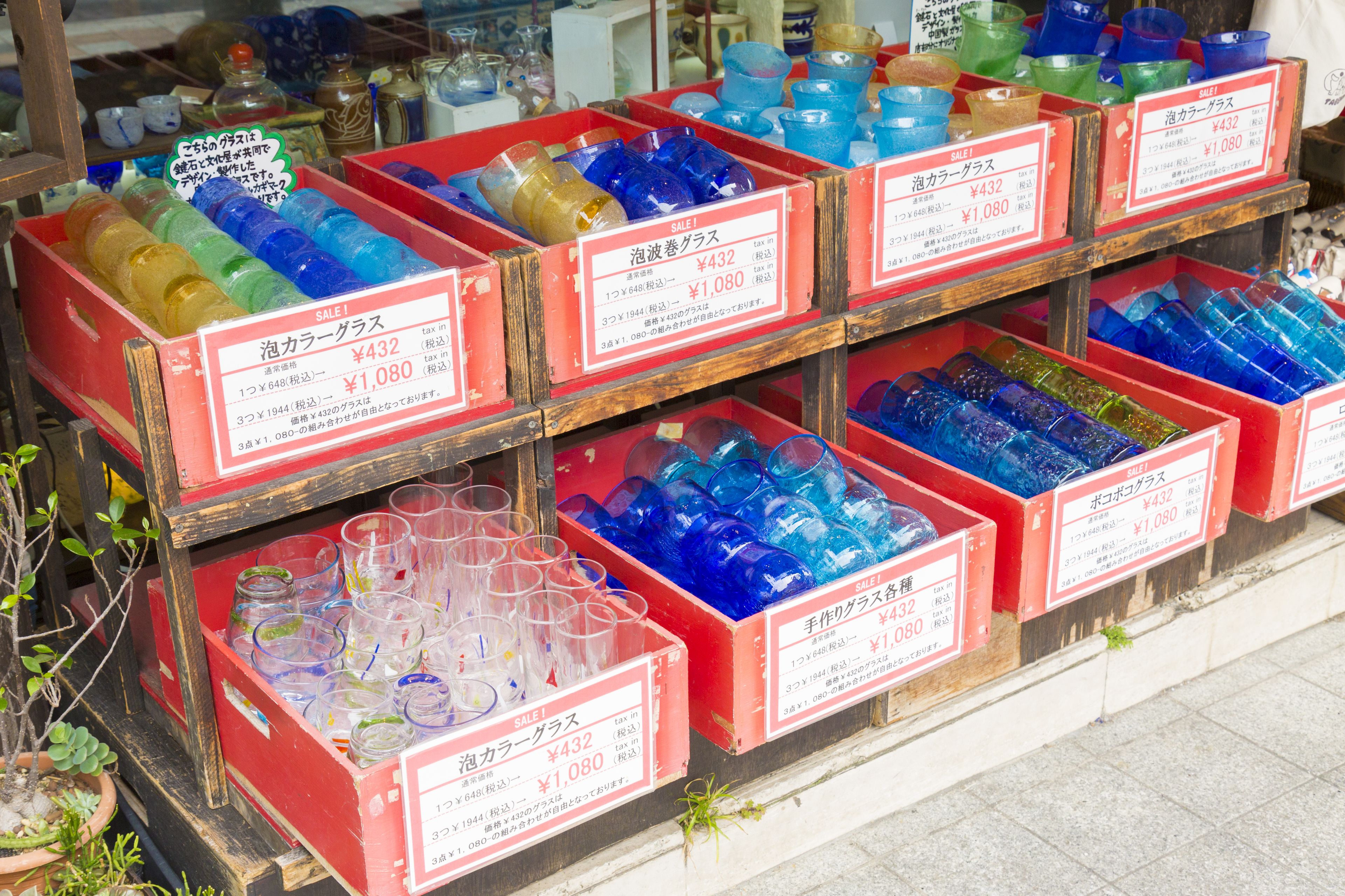 Una exhibición de frascos y recipientes de vidrio de colores a la venta, cada uno con su precio indicado.