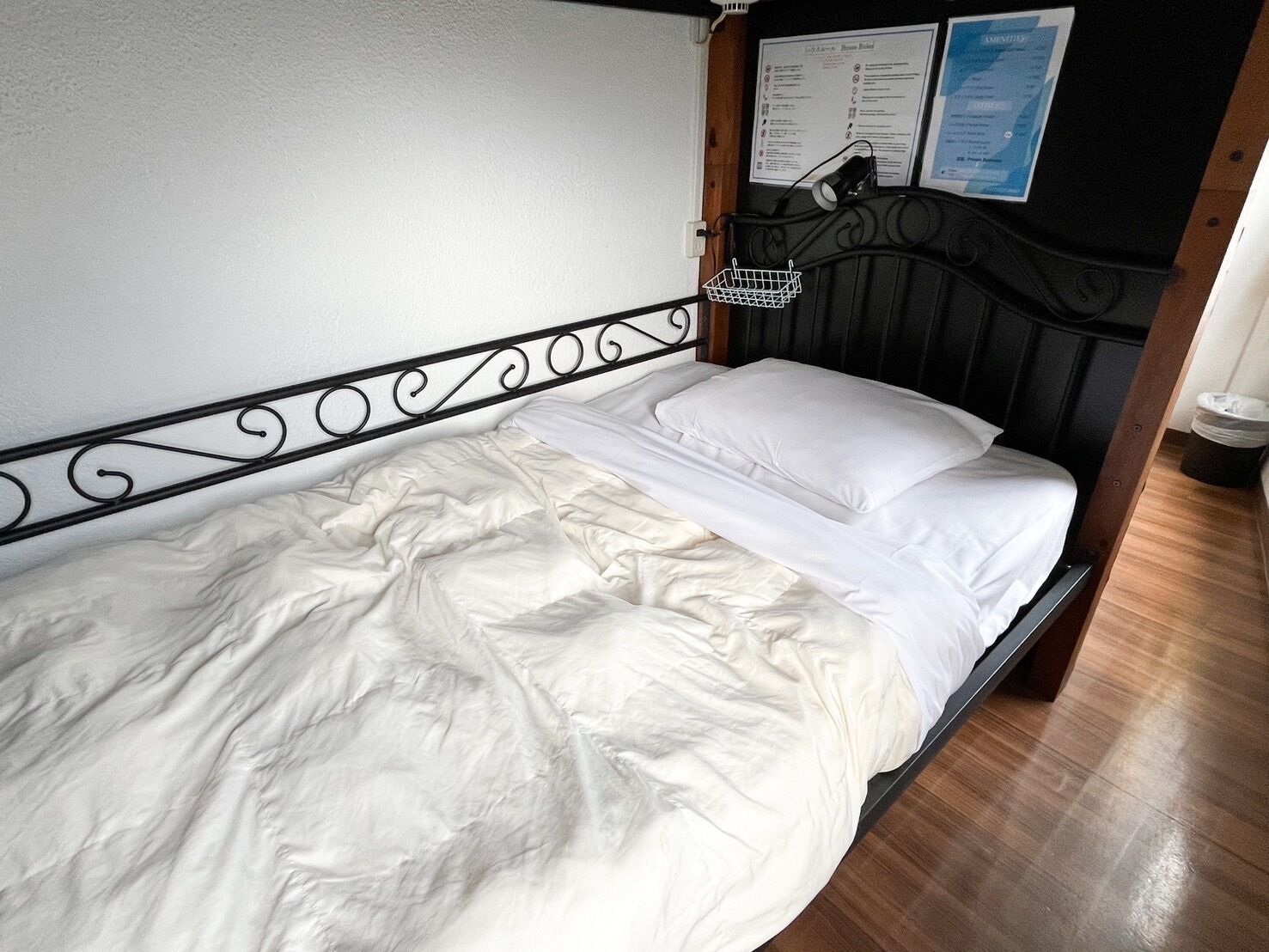 A single bed with a metal headboard, white bedding, and a small white basket on the side.
