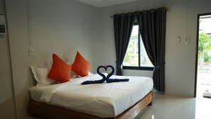 A bedroom with a wooden bed, white bedding, orange pillows, and a heart-shaped towel arrangement. - Khlong Dao Sunset Villa (Ko Lanta)
