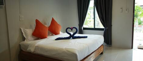 A bedroom with a wooden bed, white bedding, orange pillows, and a heart-shaped towel arrangement.