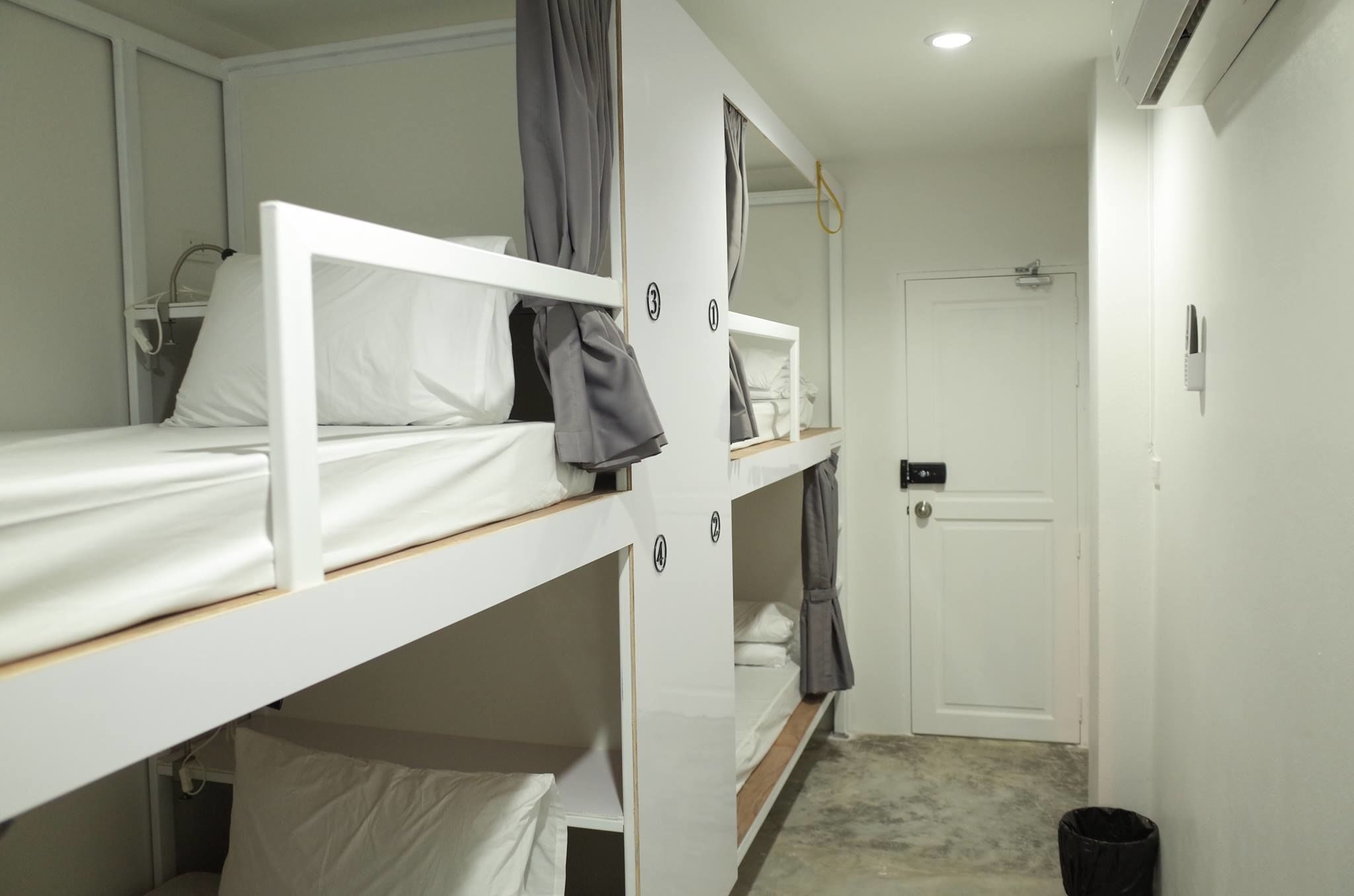 A bunk room with white beds, a door, and a small trash bin.