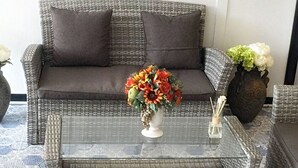 A wicker sofa with two cushions, a glass coffee table, and a vase with flowers. - Hub of Joys Hostel (Ko Lanta)