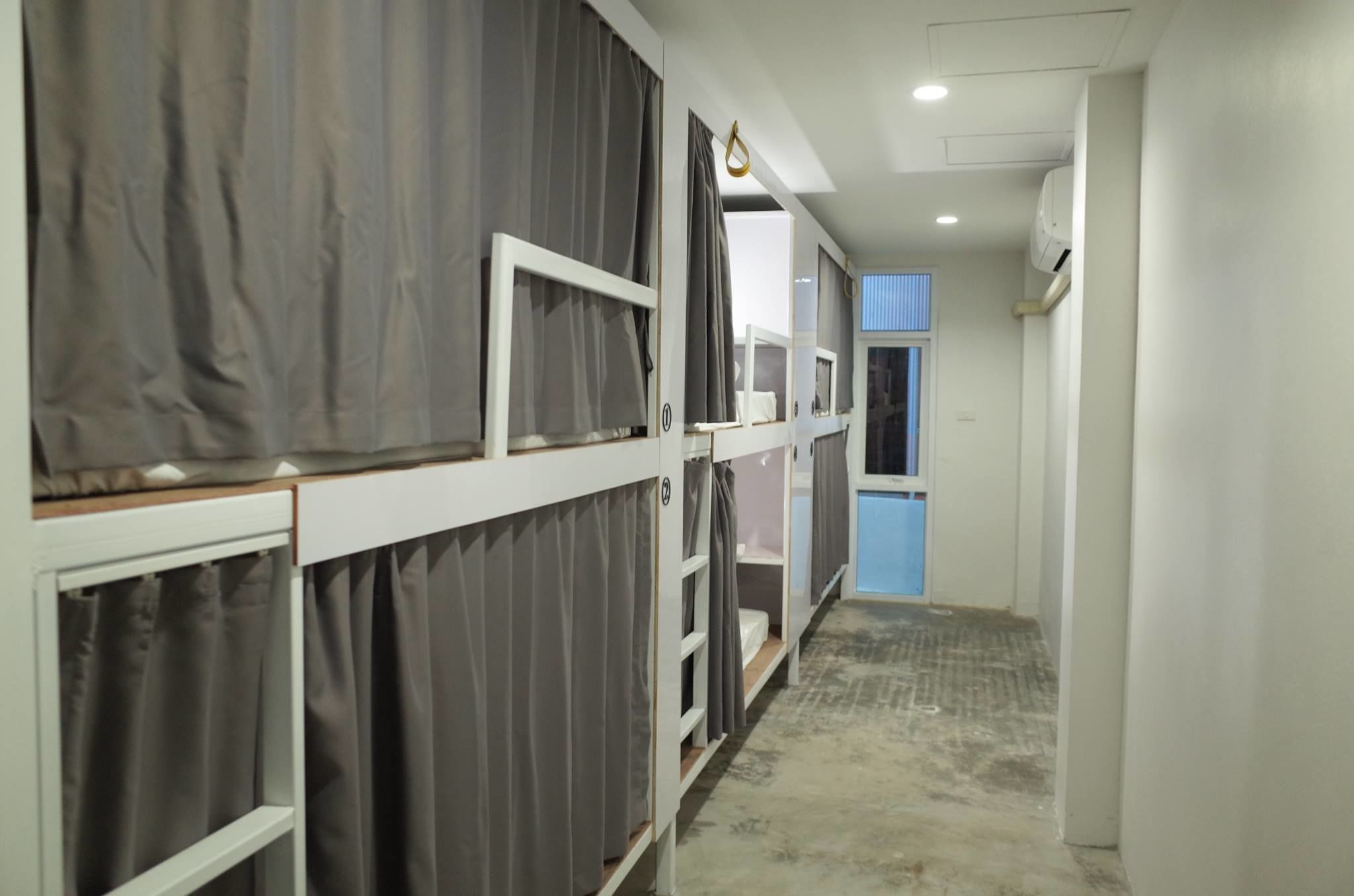 Un pasillo estrecho con literas, una puerta azul y un equipo de aire acondicionado en la pared.