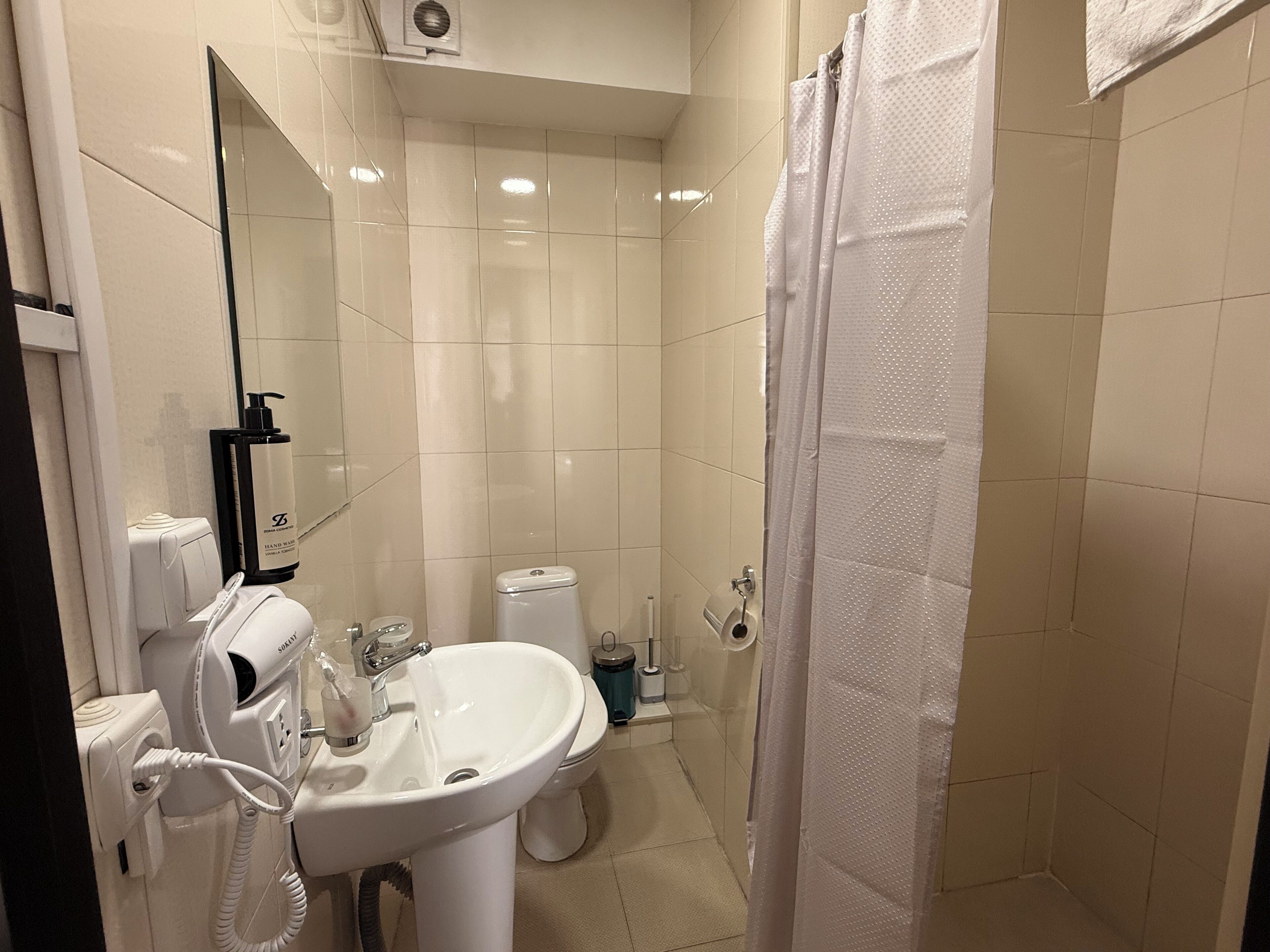 Un bagno con lavandino bianco, uno specchio, un asciugacapelli e un water.