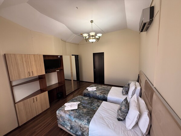 A hotel room with two beds, a TV on a wooden shelf, a ceiling fan, and a door. - Liva Hotel (Tbilisi)