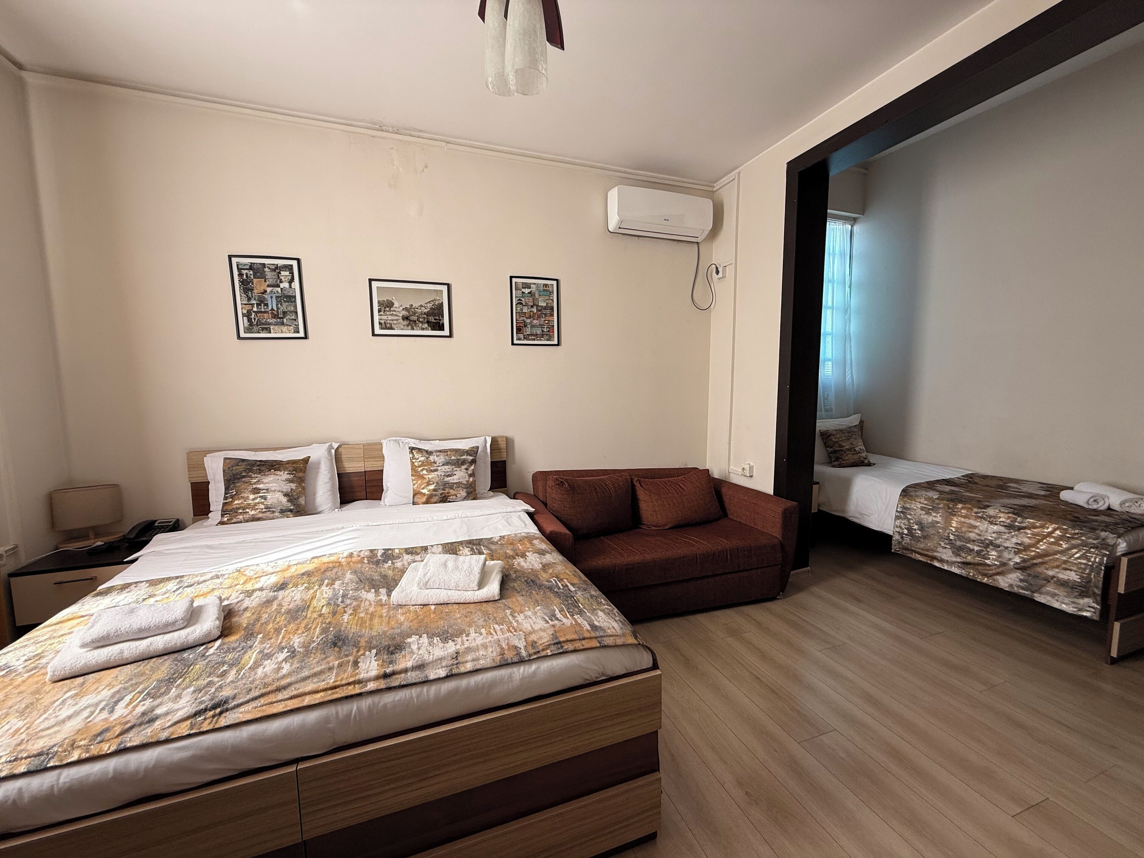 A hotel room with a large bed, a smaller bed, a sofa, and a desk. There are three framed pictures on the wall.