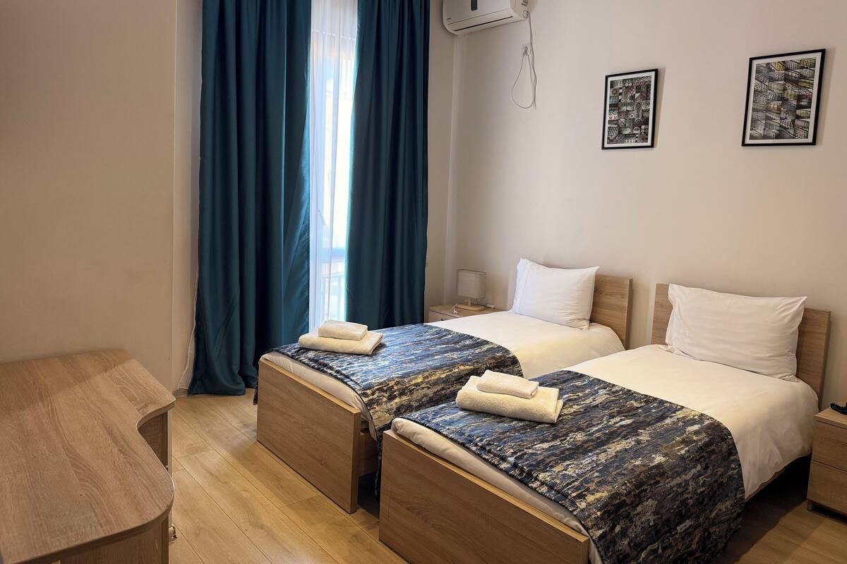 A hotel room with two beds, a desk, and an air conditioning unit.