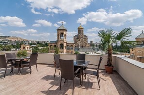 A rooftop terrace with wicker furniture and a potted plant, overlooking a historic church and cityscape. - Liva Hotel (Tbilisi)