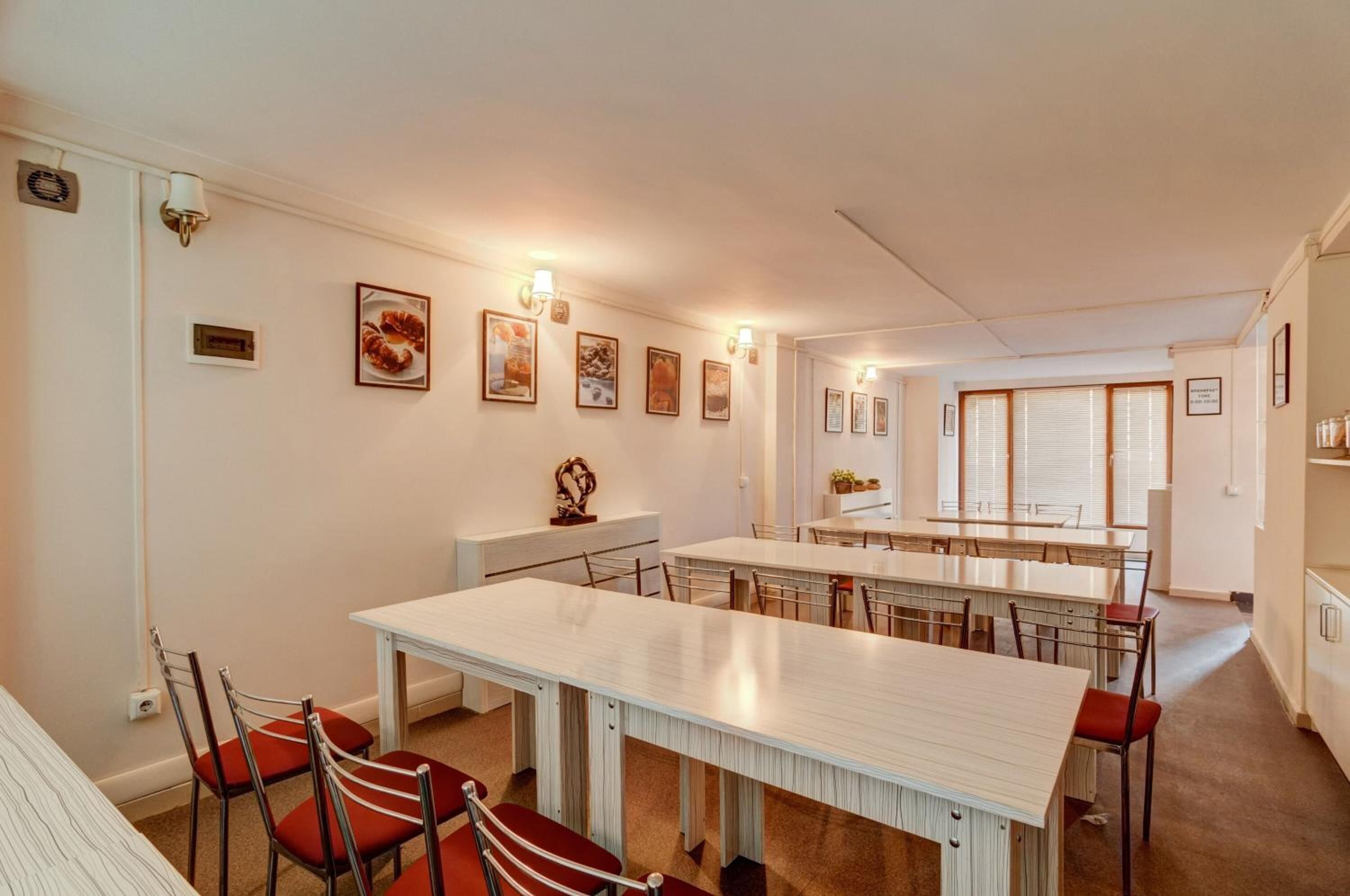 Un espace repas avec une longue table et des chaises, une petite table ornée d’un vase et des tableaux encadrés accrochés au mur.