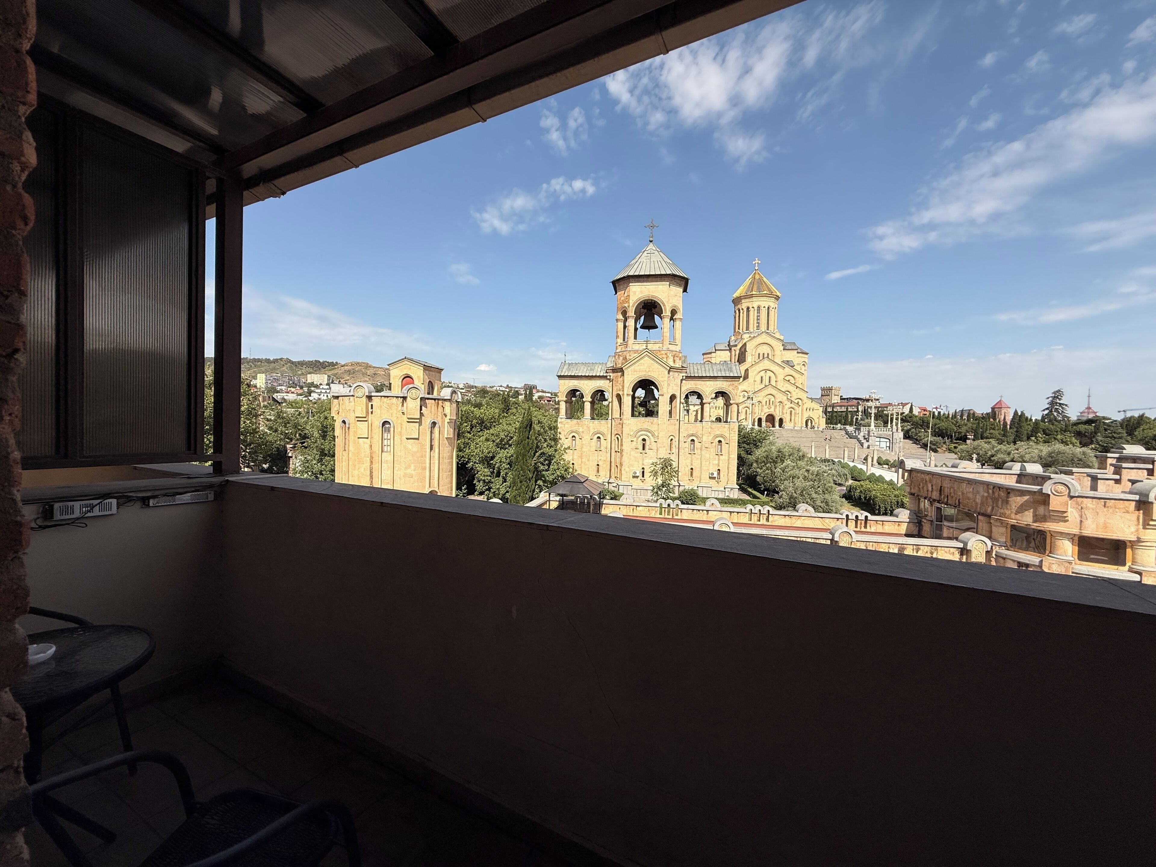 A balcony with a view of a large church with two towers and a bell tower, surrounded by buildings and trees.