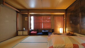 A traditional Japanese-style room with tatami flooring, a low table with cushions, a bed with a patterned blanket, and sliding doors. - Oyado Sanjo Machiya (Kyoto)