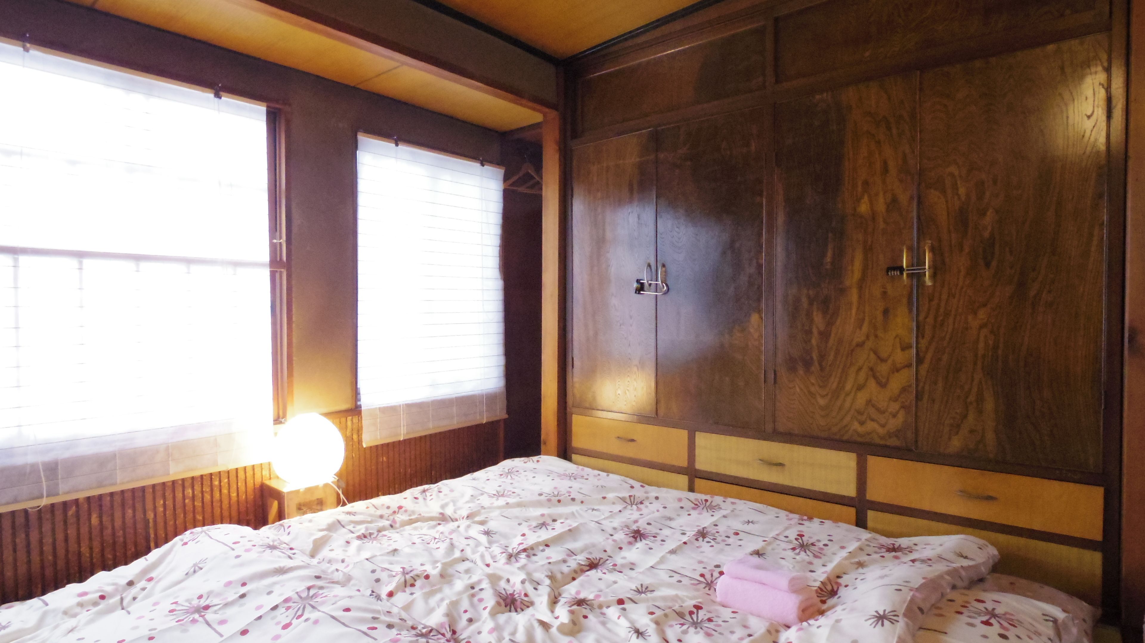 Un dormitorio con un armario de madera, una cama con ropa de cama floral y una lámpara de noche.