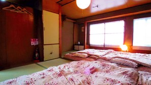 Une pièce traditionnelle japonaise avec un sol recouvert de tatamis, un futon servant de lit, un paravent shoji et une porte shoji suspendue.