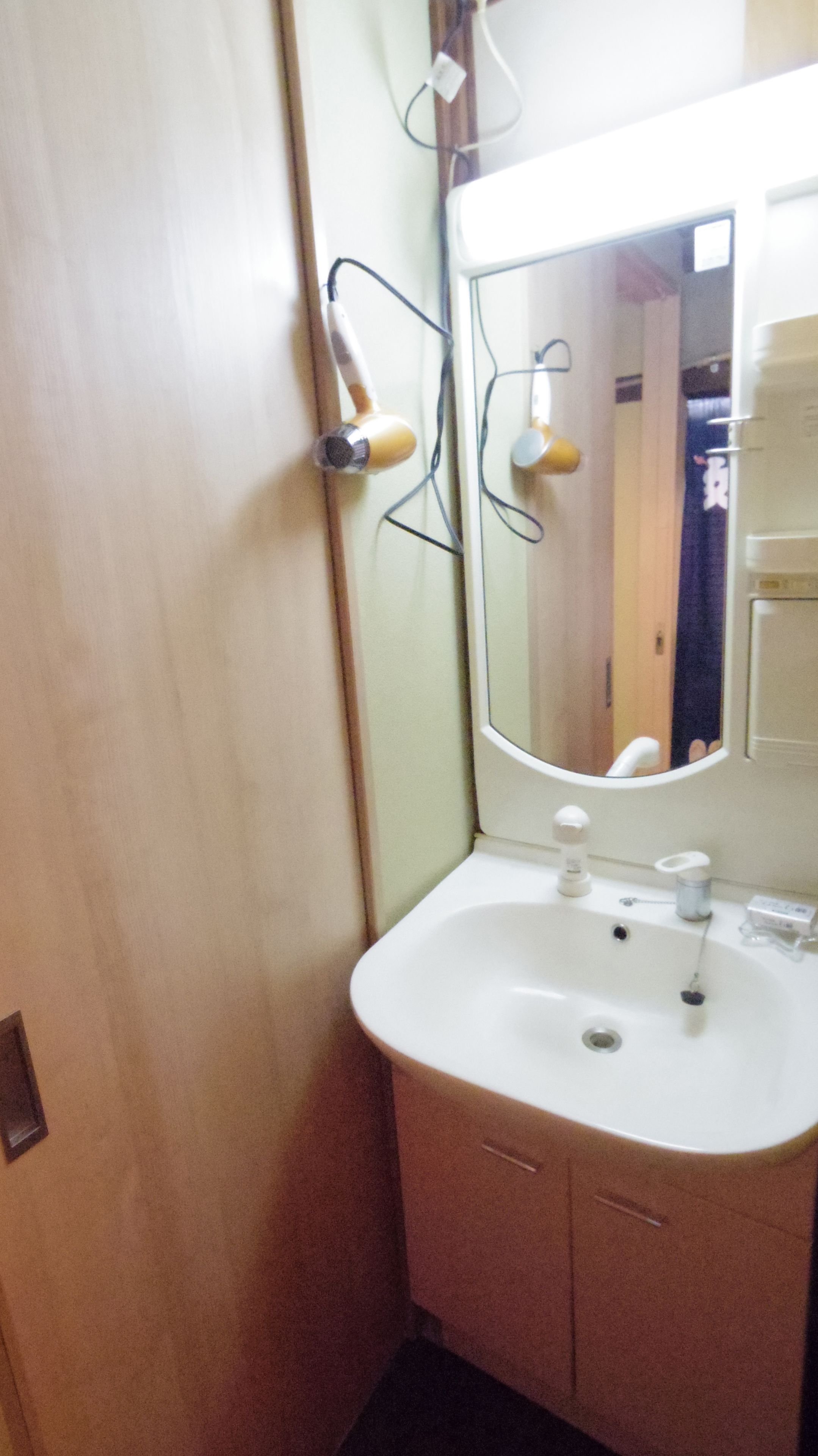 Ein Badezimmer mit einem weißen Waschbecken, einem Spiegel und zwei an der Wand befestigten Haartrocknern.