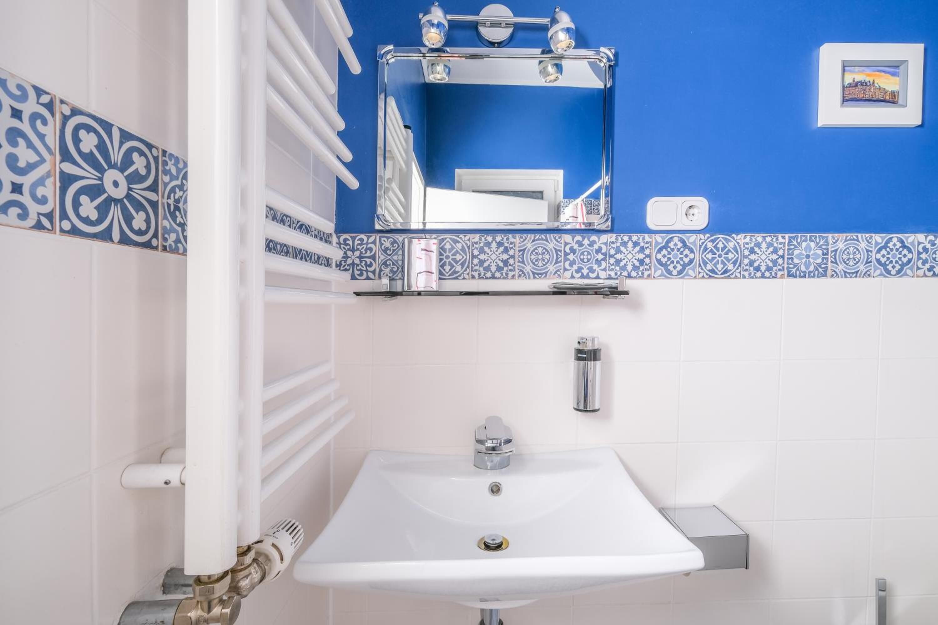 Ein Badezimmer mit einem weißen Waschbecken, blauen und weißen Fliesen mit Muster, einem Spiegel und einem Bild an der Wand.