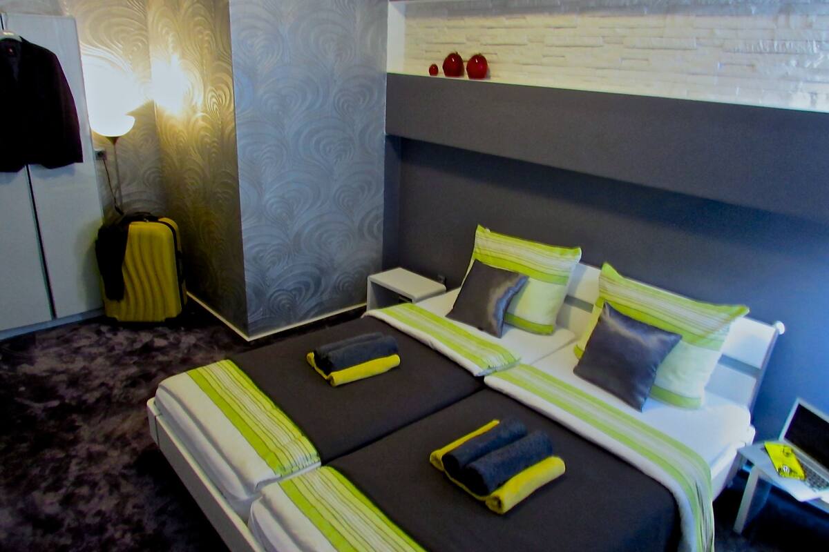 Quarto de hotel com uma cama, mesas de cabeceira, uma luminária e uma mala.