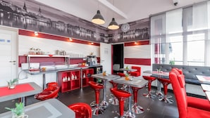 Een modern restaurantinterieur met rode en grijze zitplaatsen, een keukenhoek en een stadsmuur op de muur.